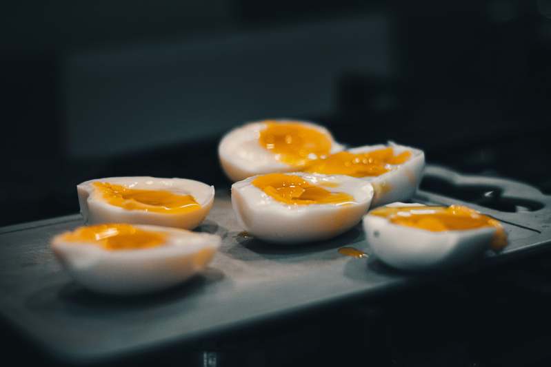 Two people in aprons testing an egg boiler side-by-side in a well-lit home kitchen, smiling and holding boiled eggs